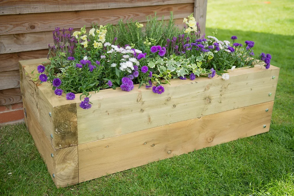 8 Simple DIY Home Projects For Beginners -DIY wooden garden planter box filled with purple and white flowers, ideal for beginner-friendly garden upgrades.