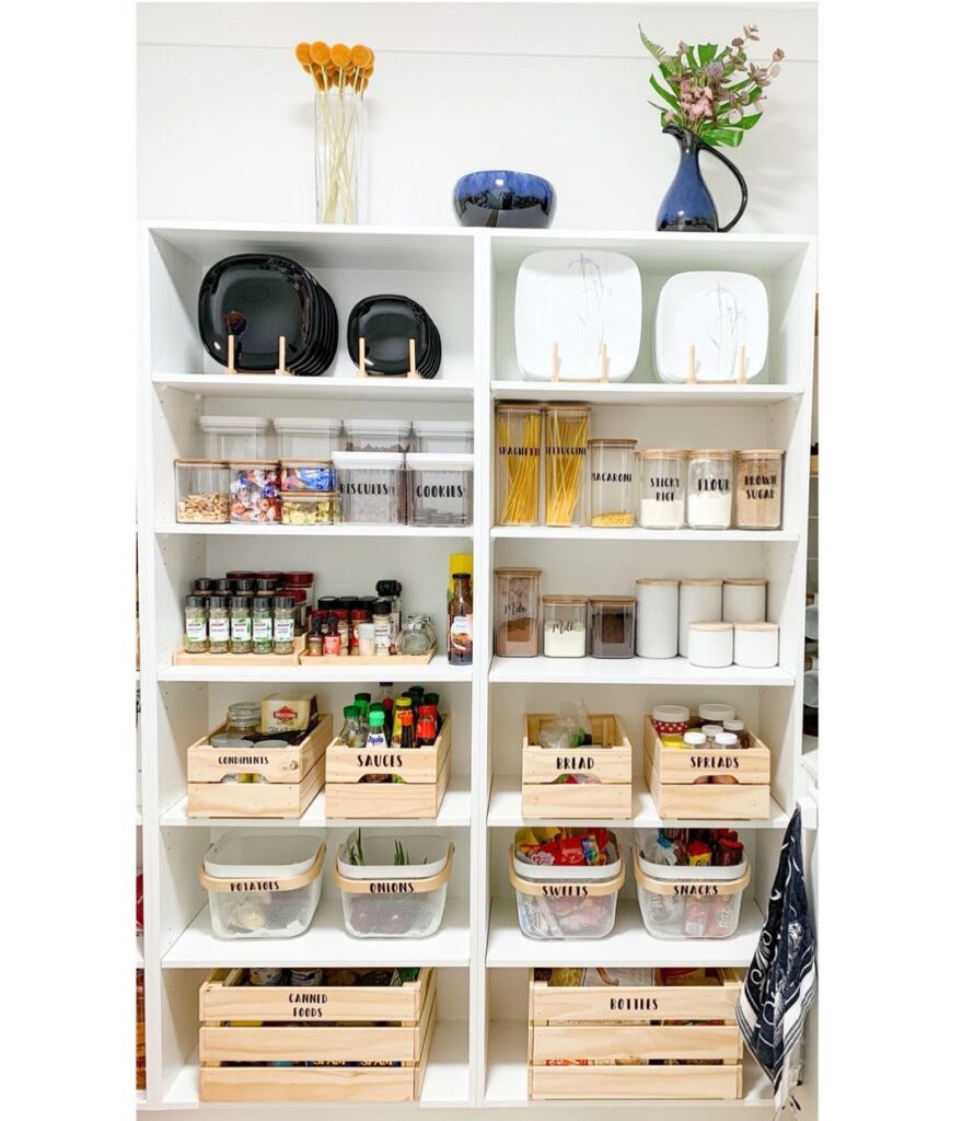 How A Kitchen Pantry Will Change Your Life - An organized kitchen pantry with labelled wooden crates, jars, and containers for storing spices, pasta, canned goods, snacks, and other essentials. wooden crates, jars, and containers for storing spices, pasta, canned goods, snacks, and other essentials.