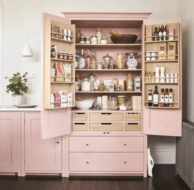 How A Kitchen Pantry Will Change Your Life -Freestanding pink pantry cabinet with organized wooden shelves, drawers, and spice racks, filled with various pantry items, spices, and cooking essentials.