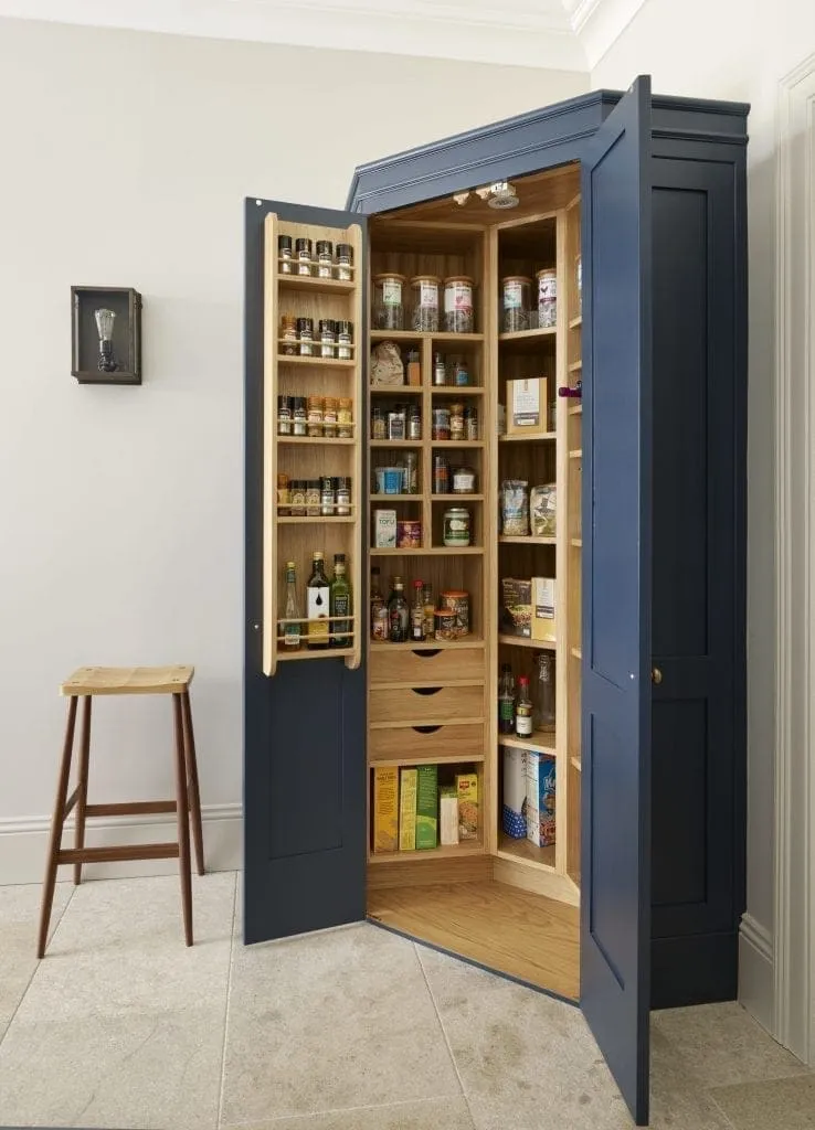 How A Kitchen Pantry Will Change You Life - Freestanding corner pantry cabinet with navy blue doors, featuring organized wooden shelves stocked with spices, canned goods, and pantry items, perfect for maximizing kitchen storage.