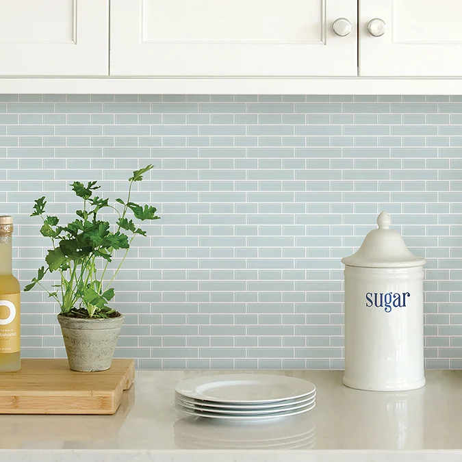 8 Simple DIY Home Projects For Beginners - Sea Glass peel and stick backsplash in a kitchen with white cabinets, potted herb plant, and vintage sugar canister